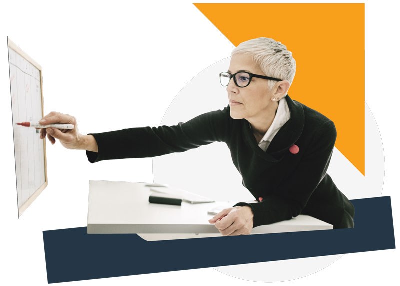 Woman leaning over a desk to write on a whiteboard with a red marker.