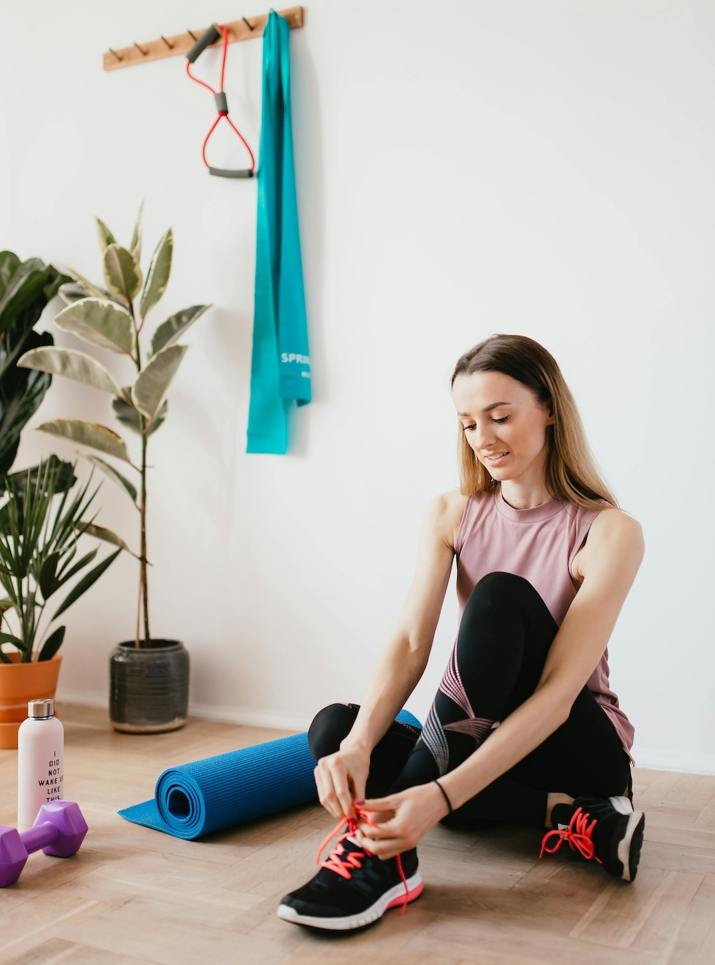 Woman sits on the floor of a yoga studio to tie her sneakers.