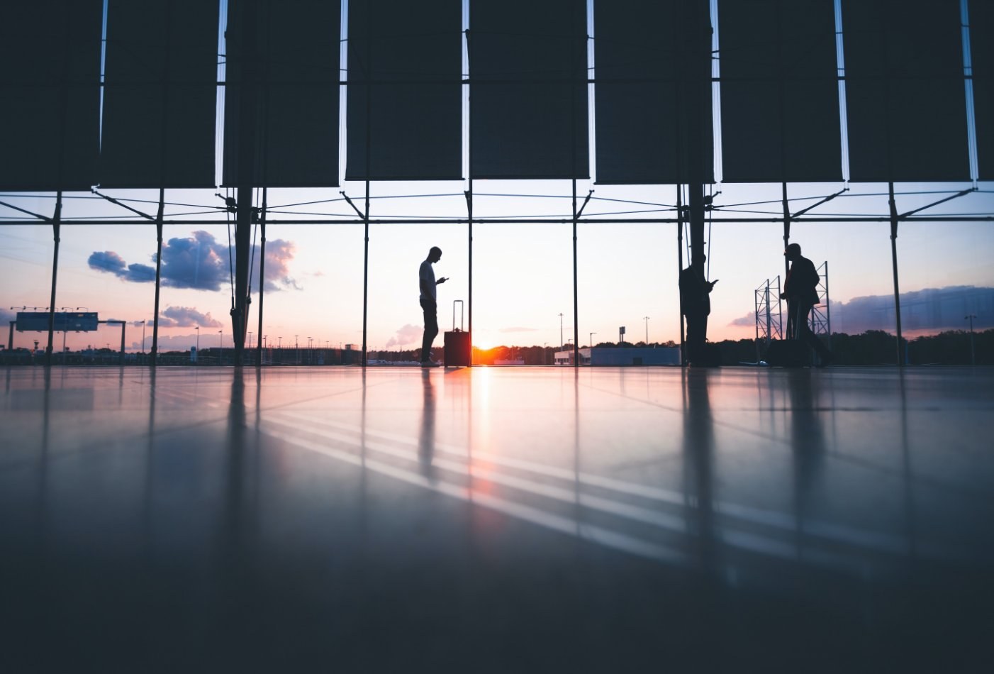 a person standing in an airport with windows behind showing sunset or sunrise
