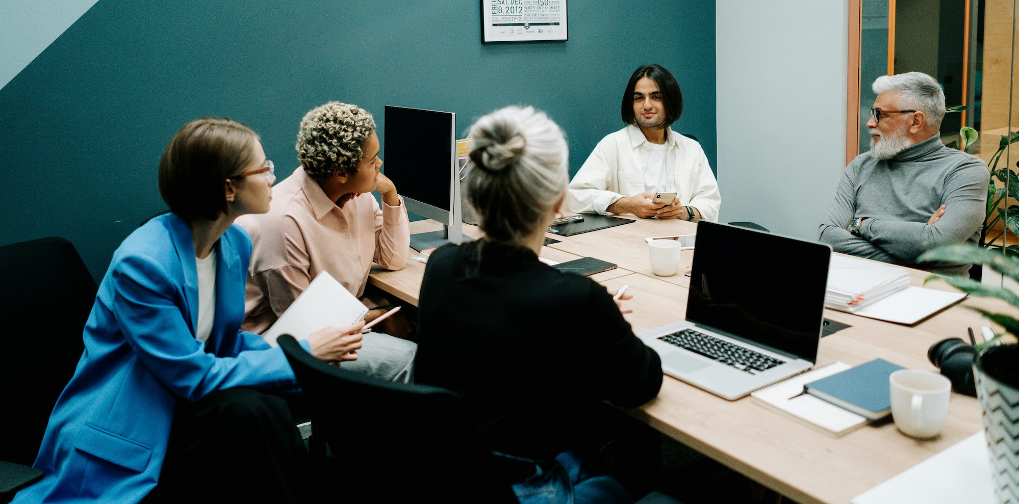 A group of 5 people congregate in an office to have a discussion.
