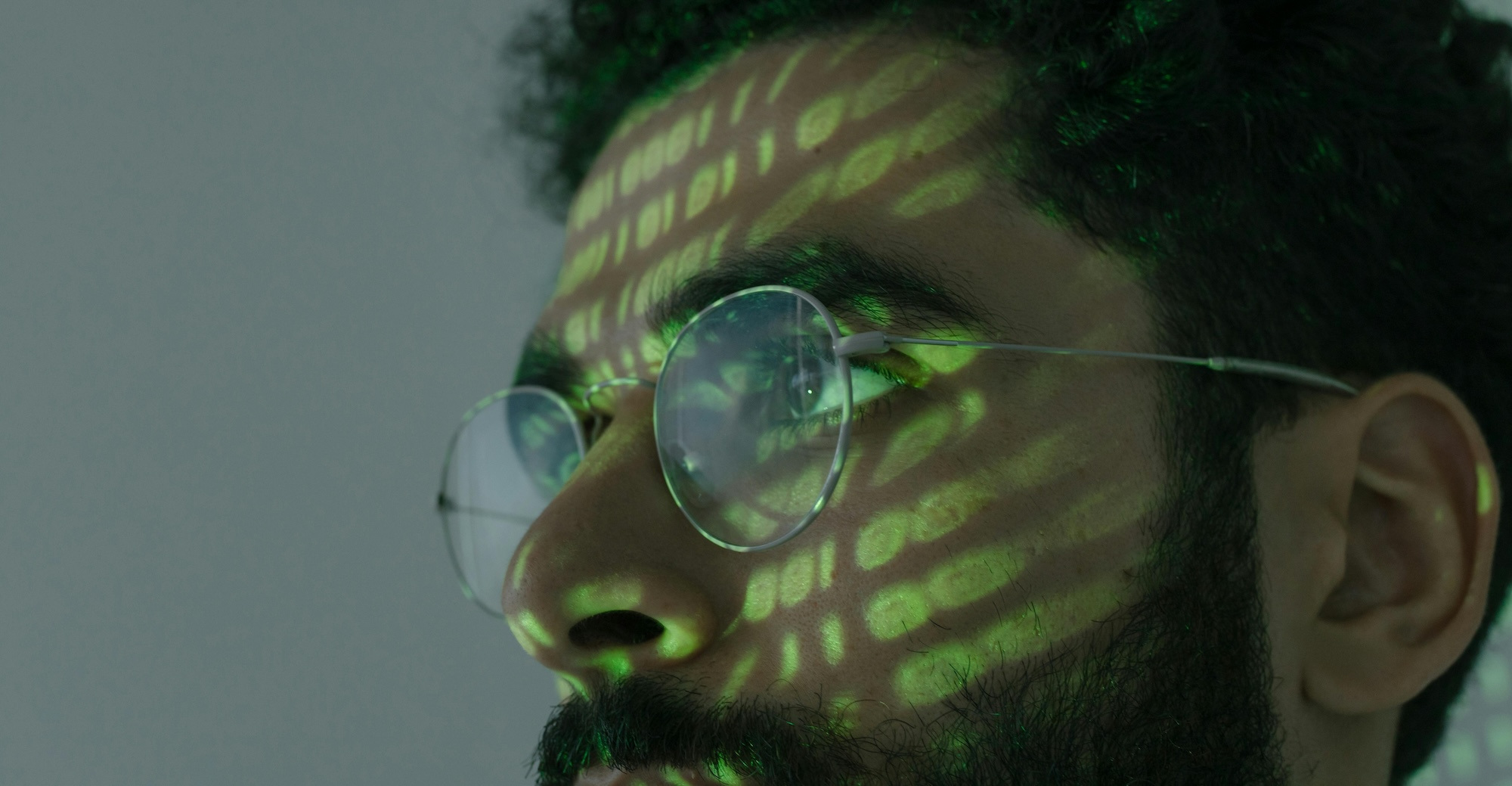 A close-up of a man's face with yellow-green light projecting binary code on his face