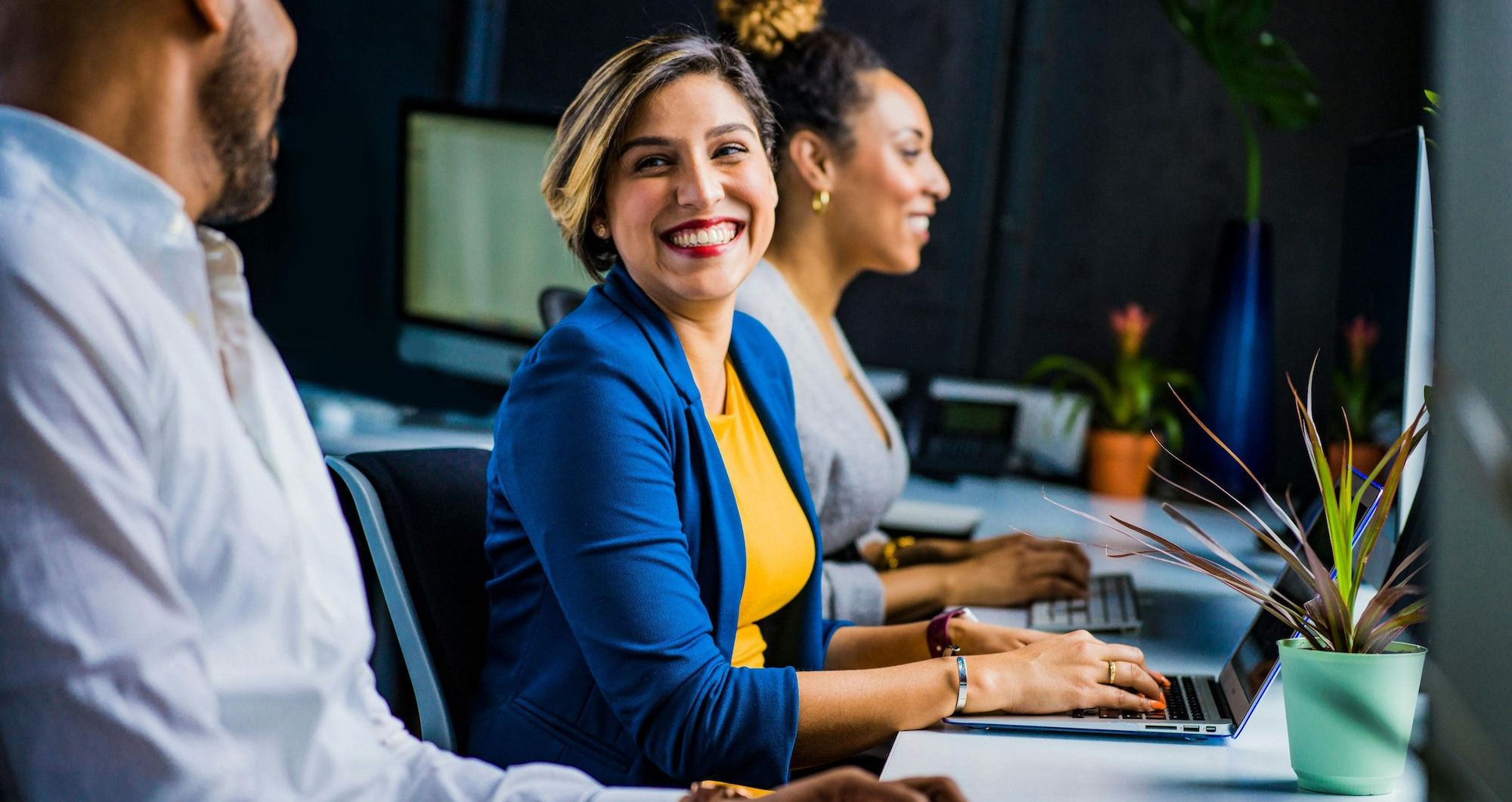 Woman smiles at a man sitting next to her in an office while typing on her laptop.