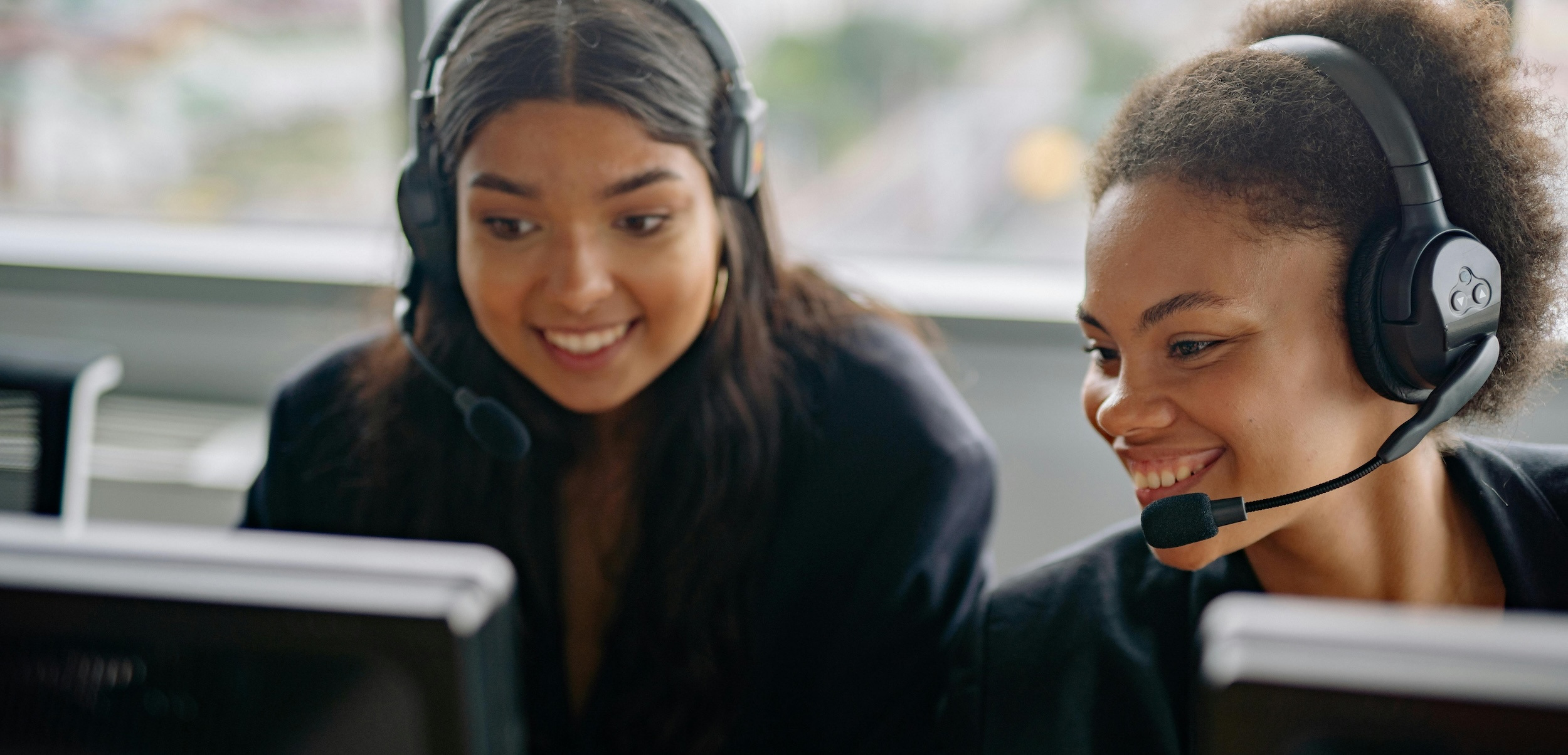 Two women smile wearing headsets inside of a call center.