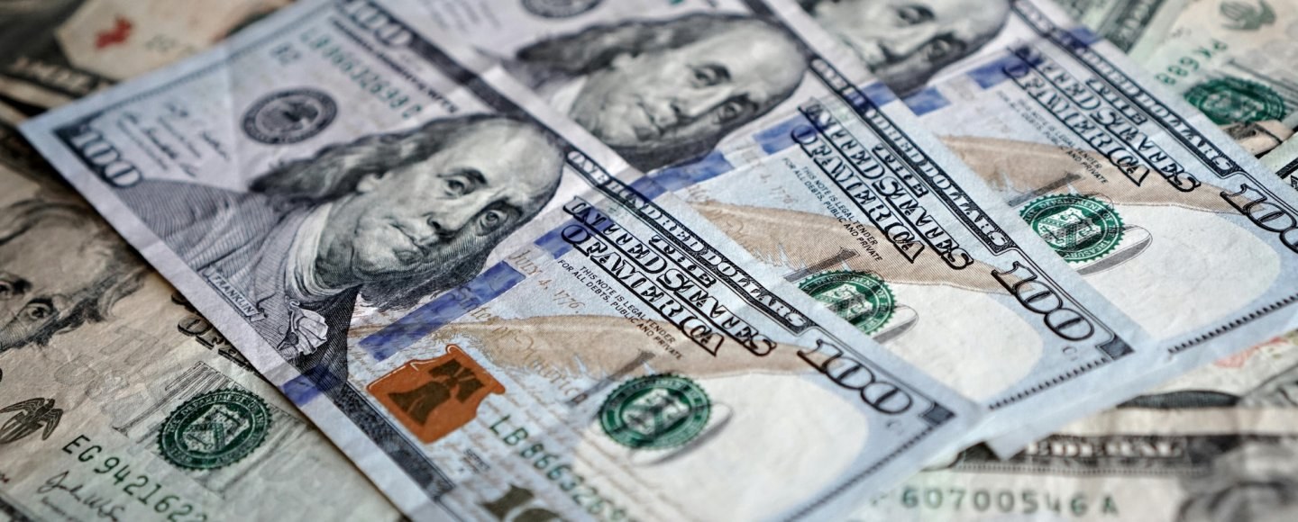 Three U.S. hundred dollar bills sit at the top of a pile of cash