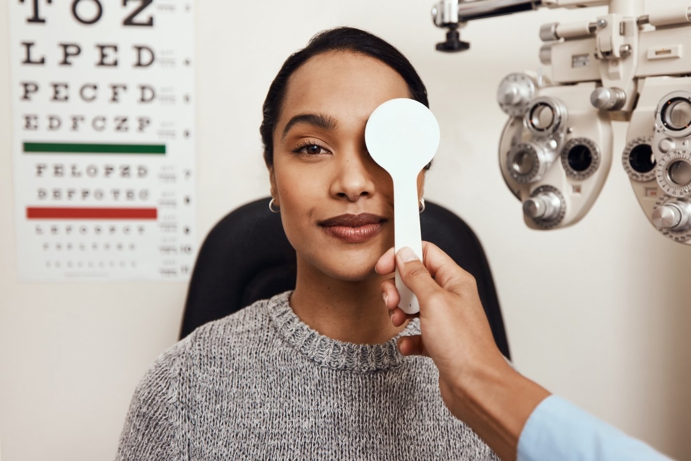 Woman sits with one eye covered by the eye doctor during a vision exam