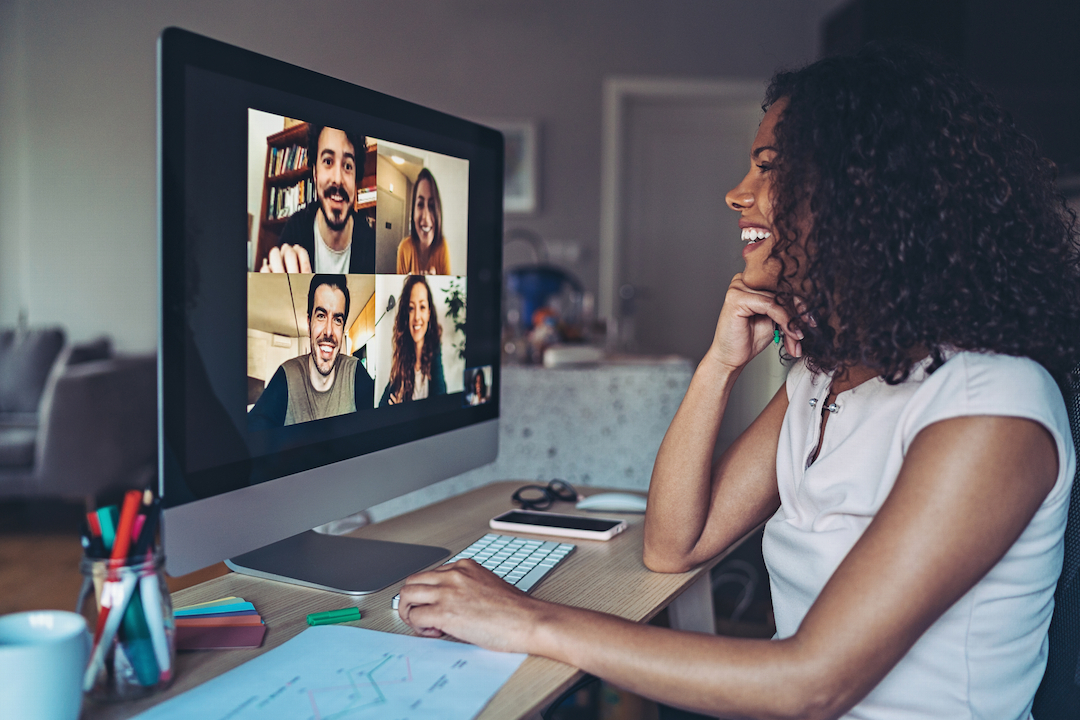 Woman smiling at a computer screen where four people are on a video call.