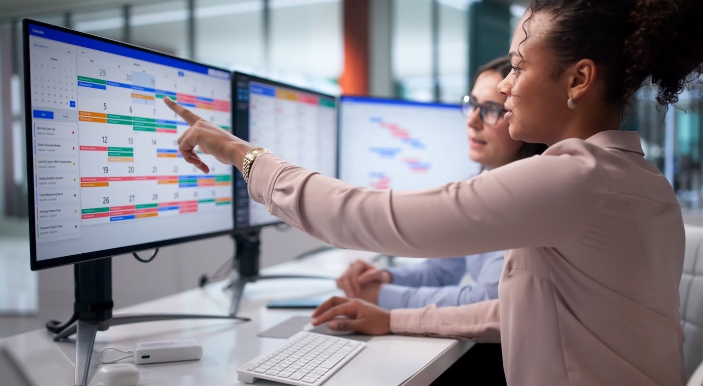Two women looking at a calendar view on an office computer screen