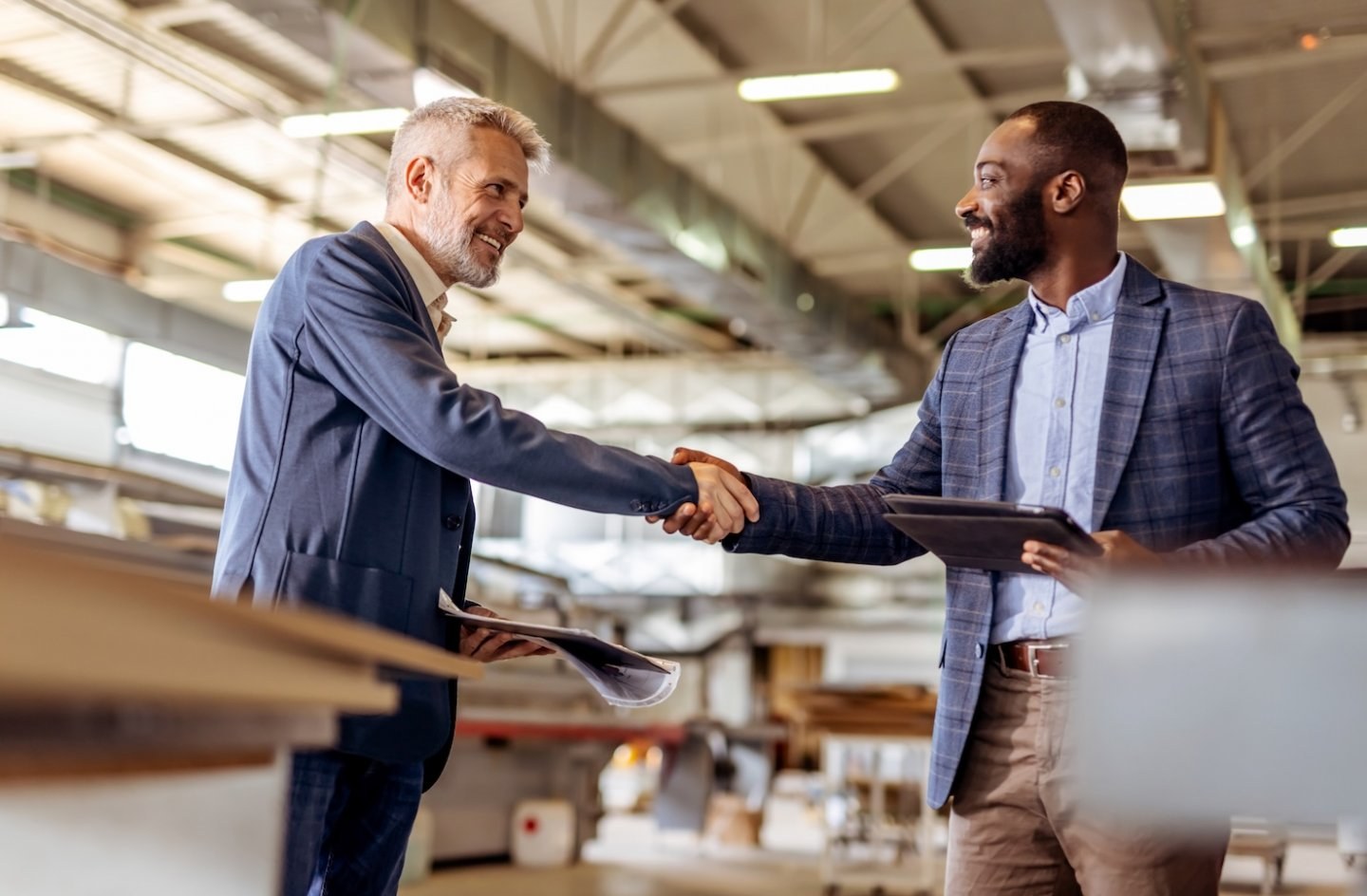 Two businessmen shake hands in industrial manufacturing workplace setting