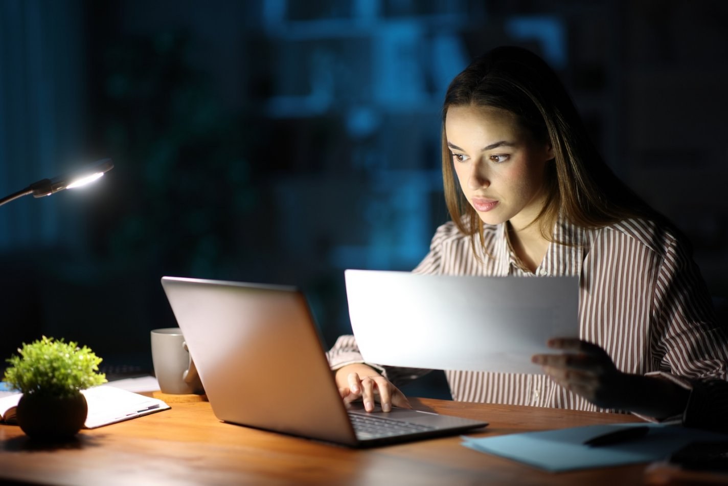 Woman catches up on work at night by desk lamp