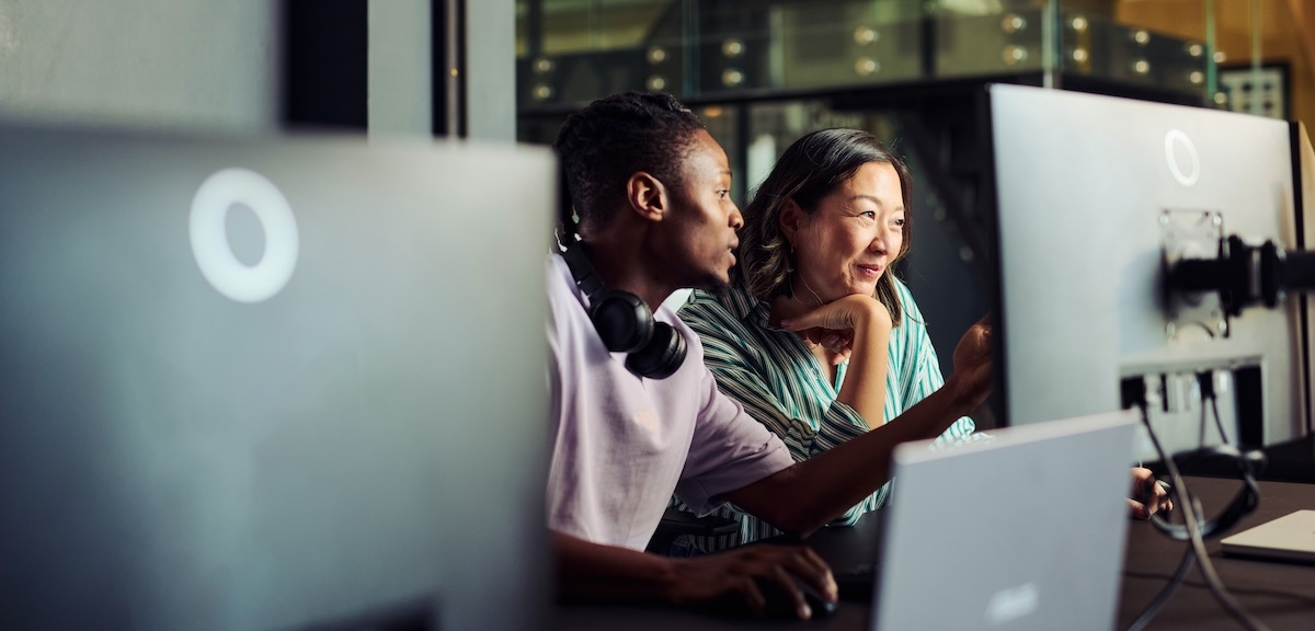 Two programmers look at a computer screen together in a tech office