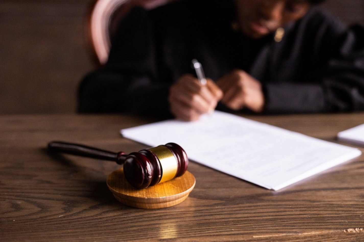 A gavel next to a person signing papers on a desk.