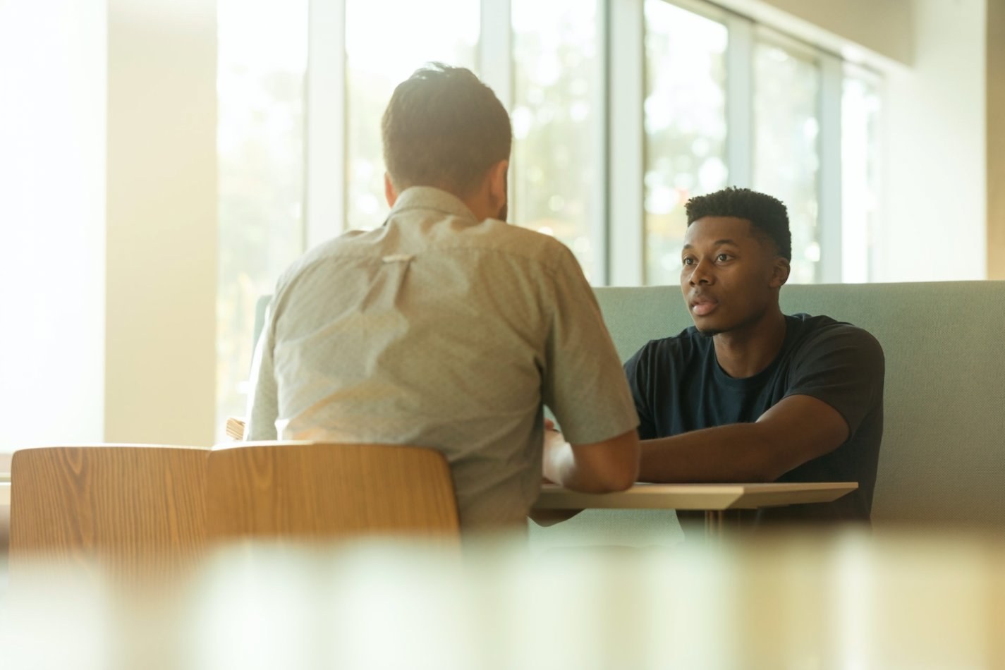 Two men sitting at a cafeteria-style booth talking