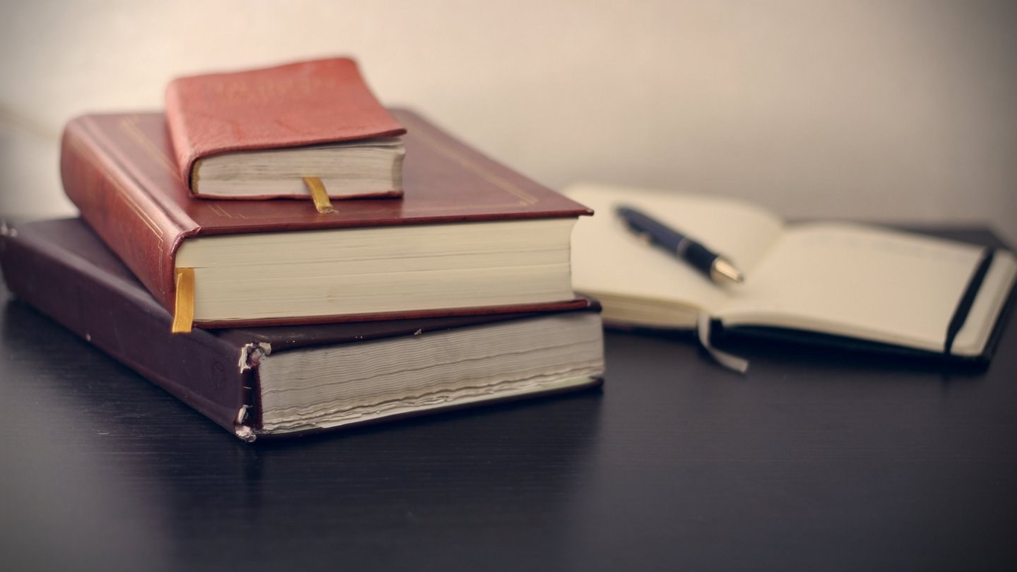 Stack of three leather bound books with an open notebook and pen to the right