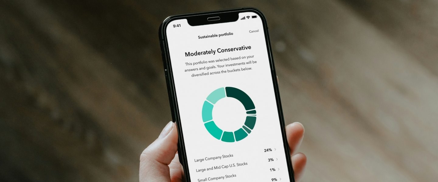 A hand holds a smartphone showing a Moderately Conservative investing portfolio on the screen.