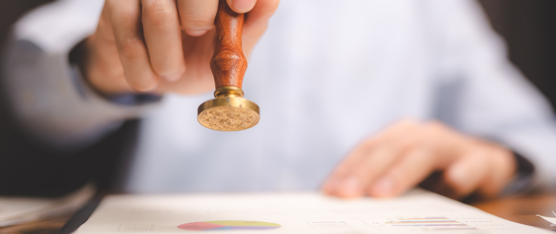 A man holds a wooden-handled notary stamp, with which he certifies a paper in front of him