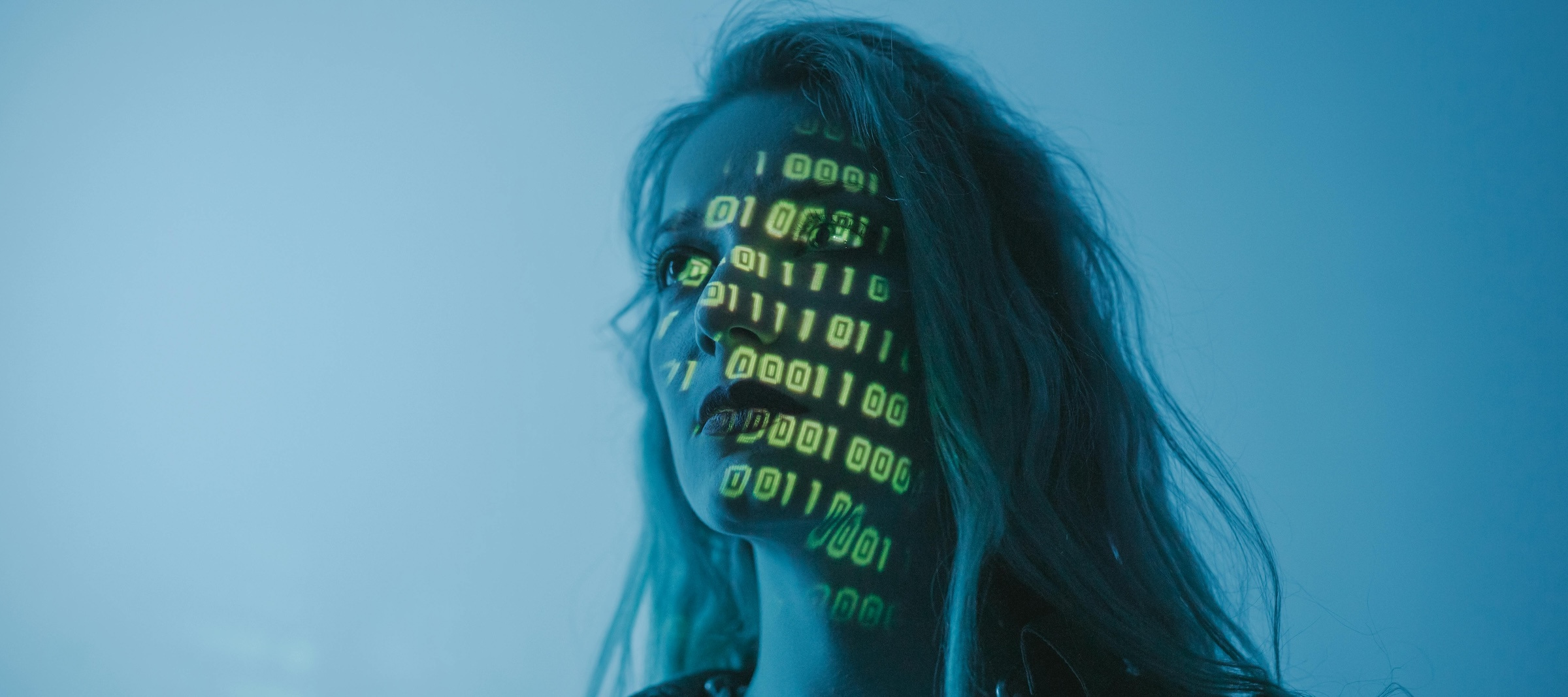 A close-up of a woman's face with binary code projected on it in green