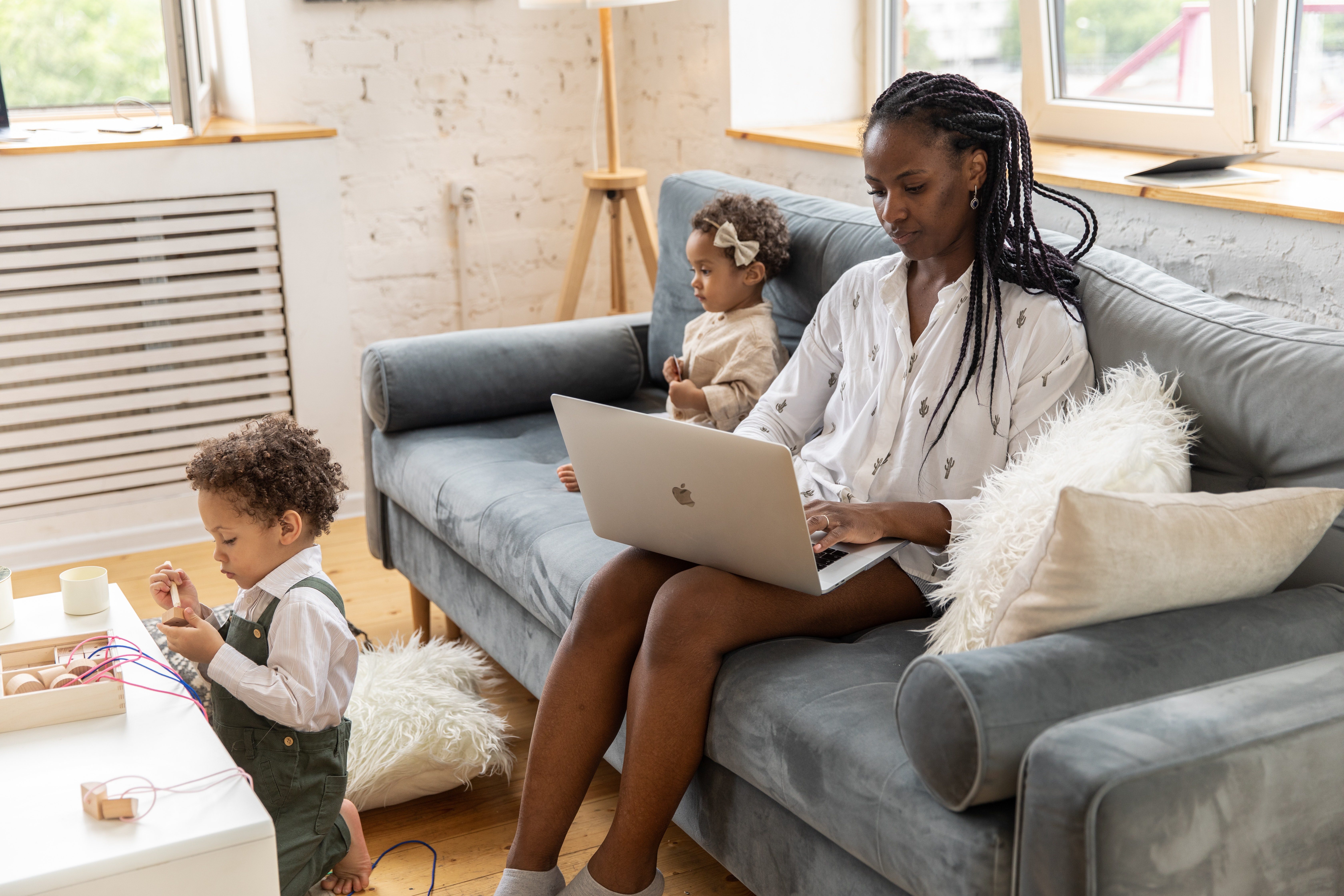 Woman working on a couch at home with kids playing next to her