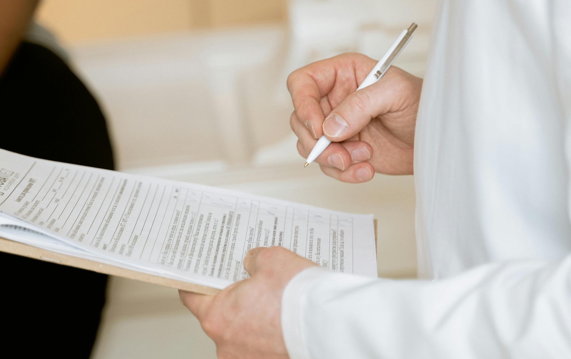 A man in a white coat fills out a form on a clipboard.
