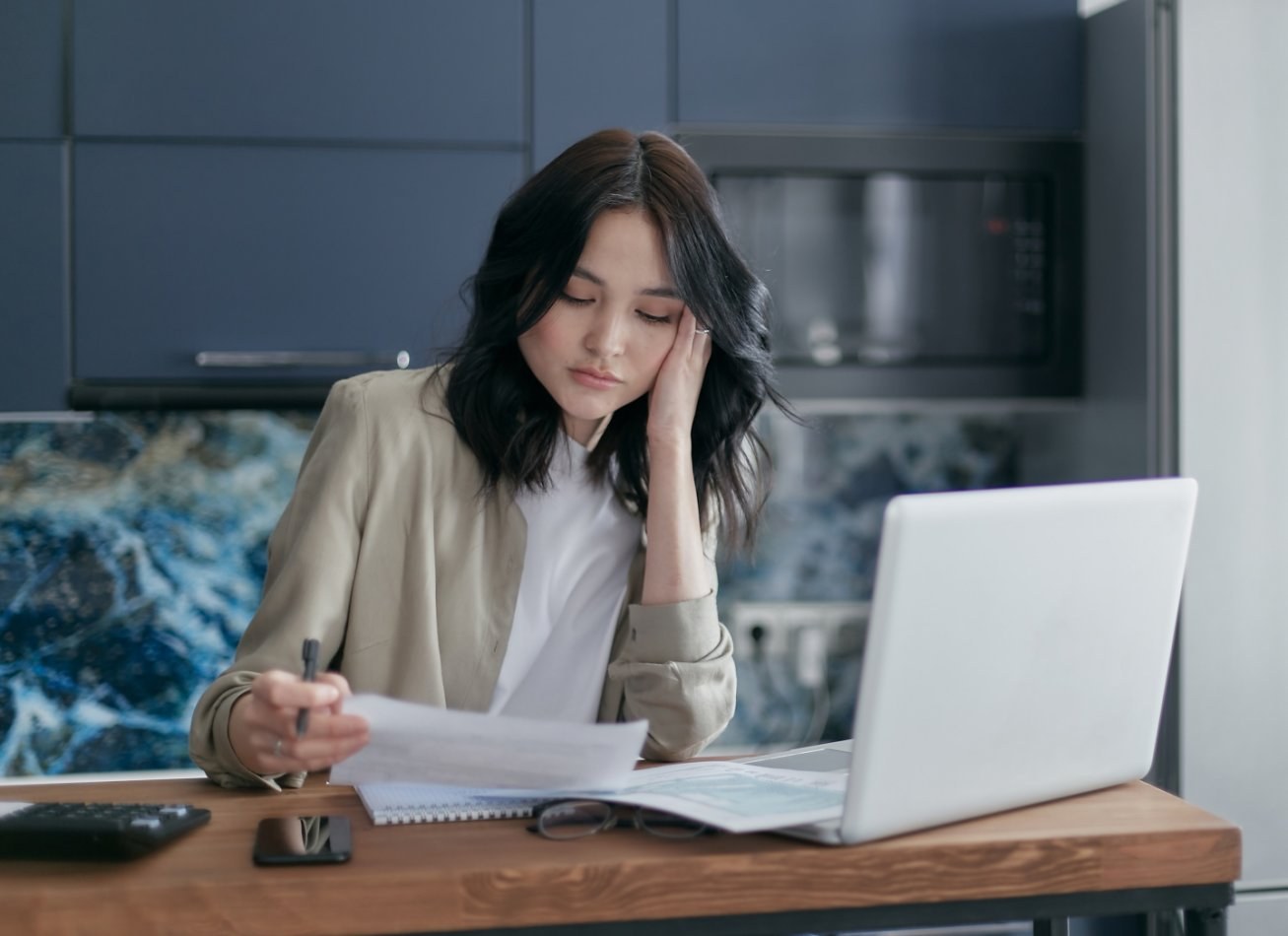 Woman looking at a piece of paper while working on a laptop