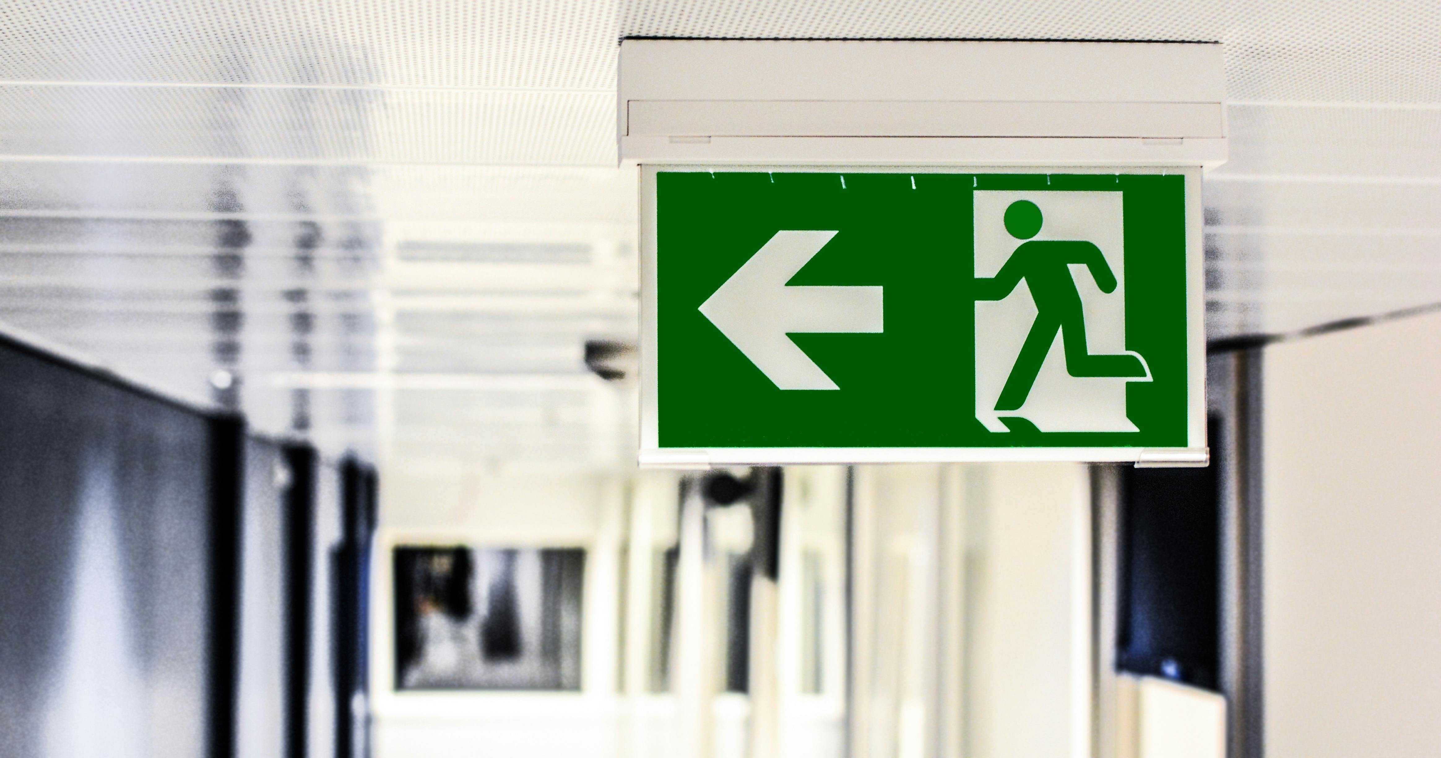 A green emergency exit signs points toward the door in a commercial building.