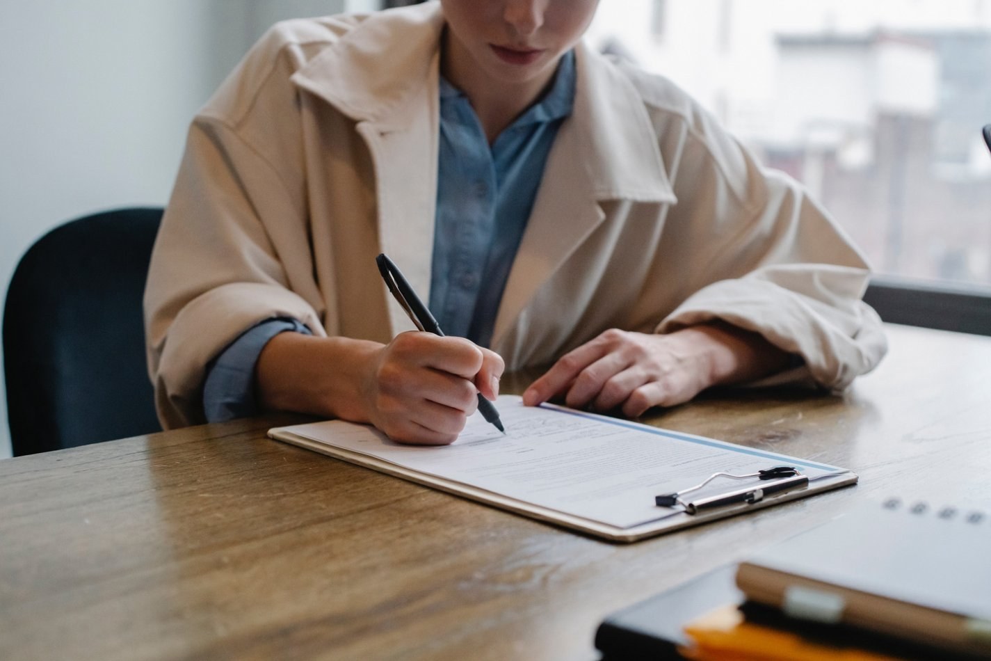 Woman sitting at a desk signing paper on a clipboard.