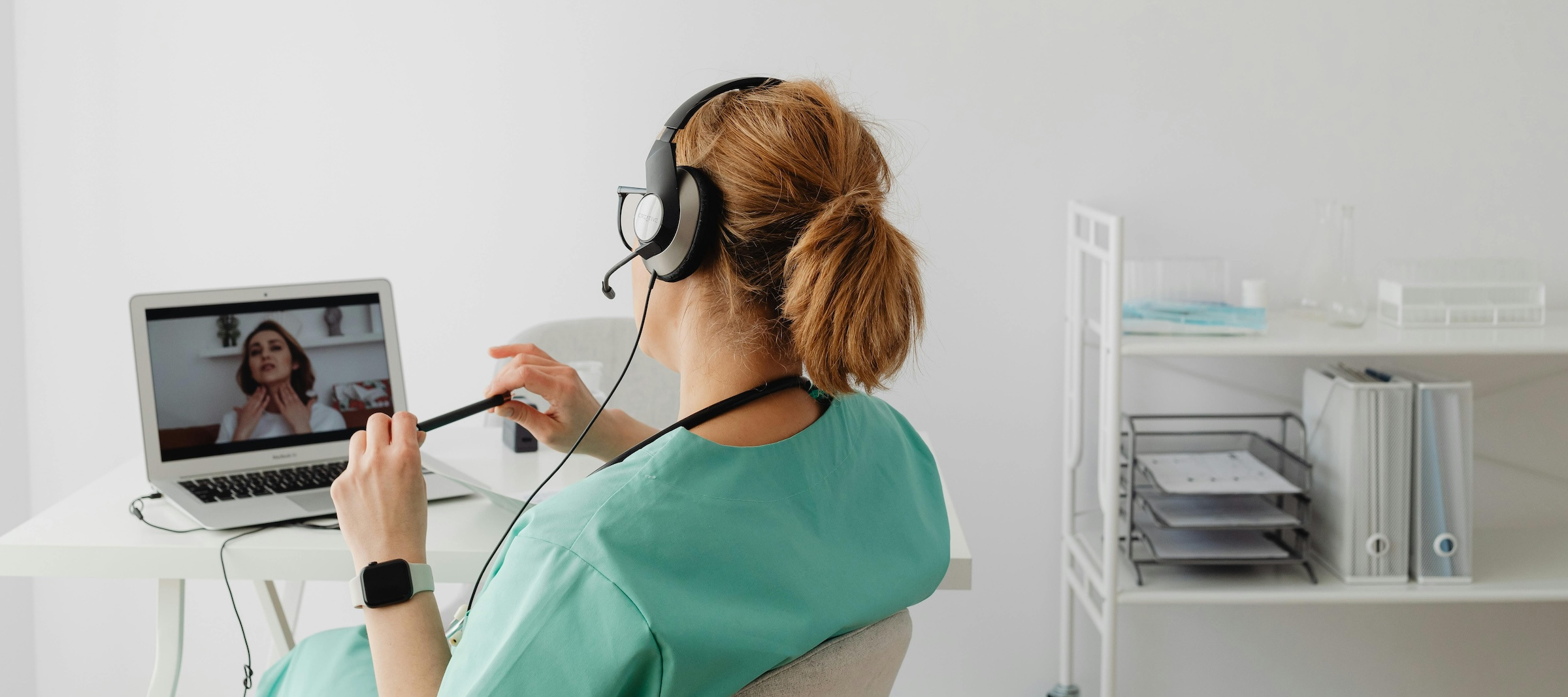 Woman on a laptop screen demonstrates to a medical provider wearing a headset in her office on a virtual visit.