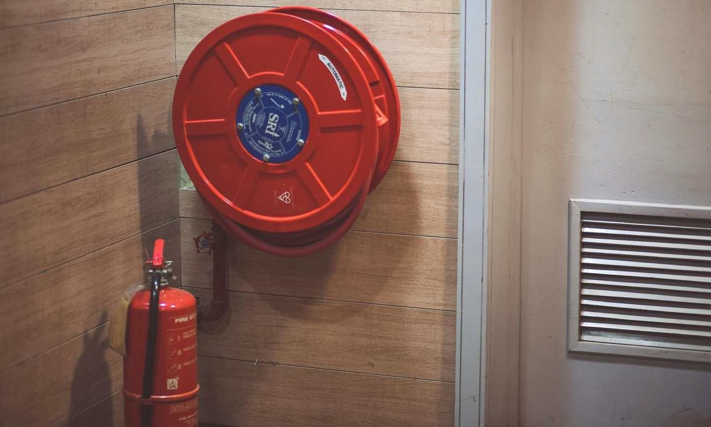 Fire extinguisher sits next to a rolled up fire hose mounted on a wall.